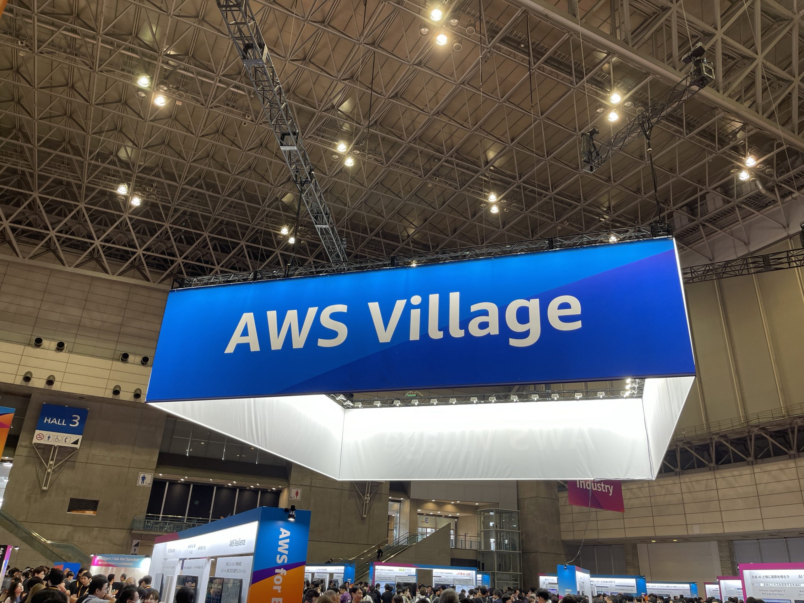 AWS Summitの会場内に設置されたAWS Villageの大型看板とブース。多数の来場者がブースを見学している様子